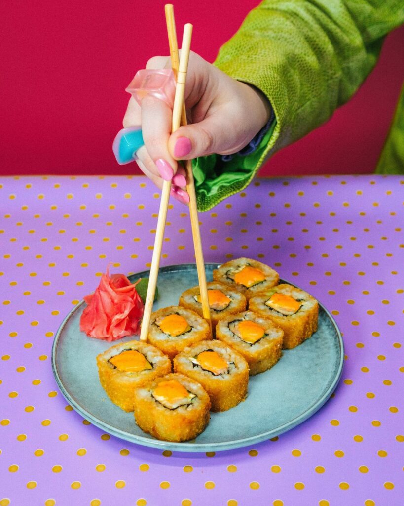 Fried sushi rolls lifted with chopsticks on a purple polka-dot table